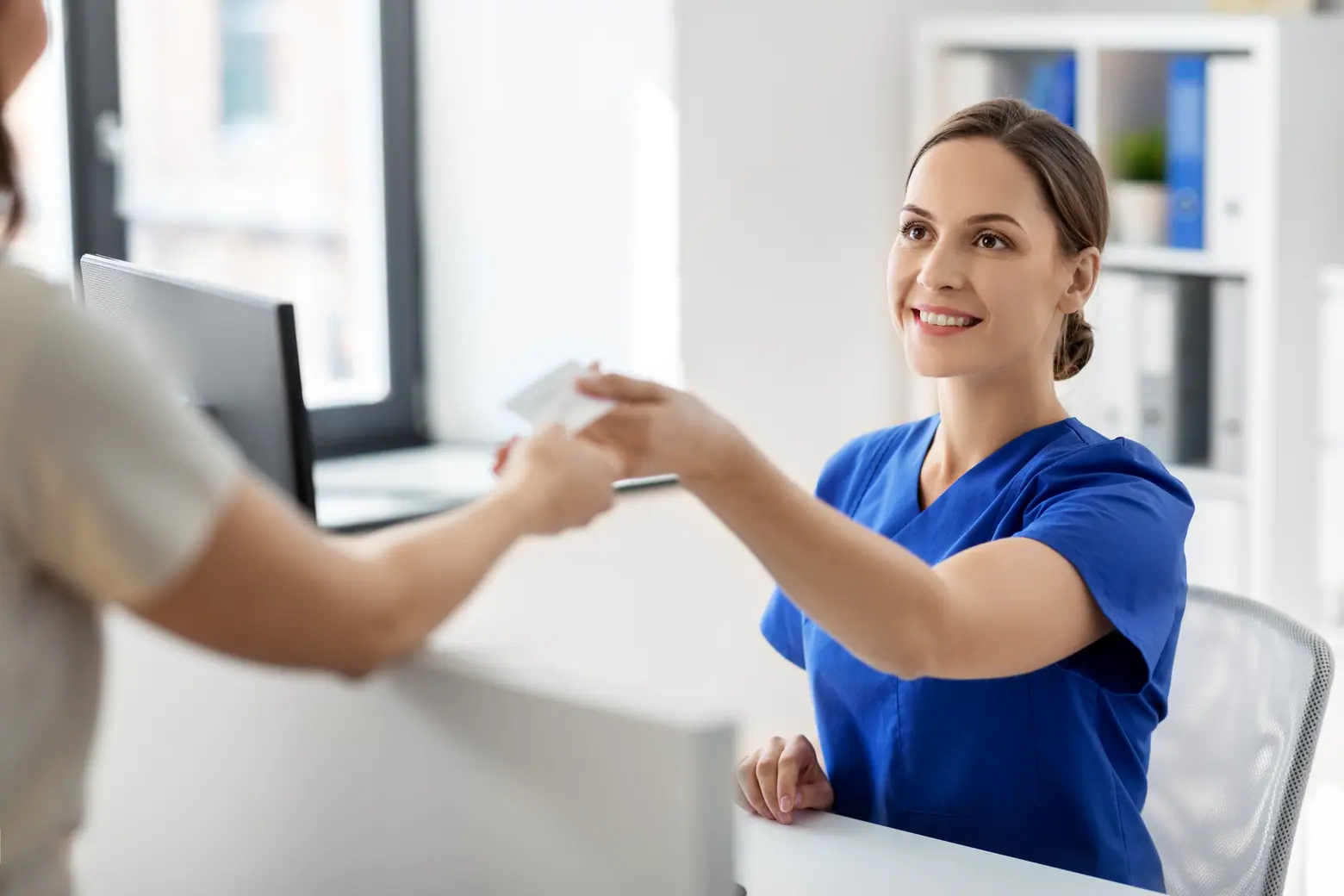 Recepcionista recebe cartão de paciente durante consulta sobre o valor da blefaroplastia
